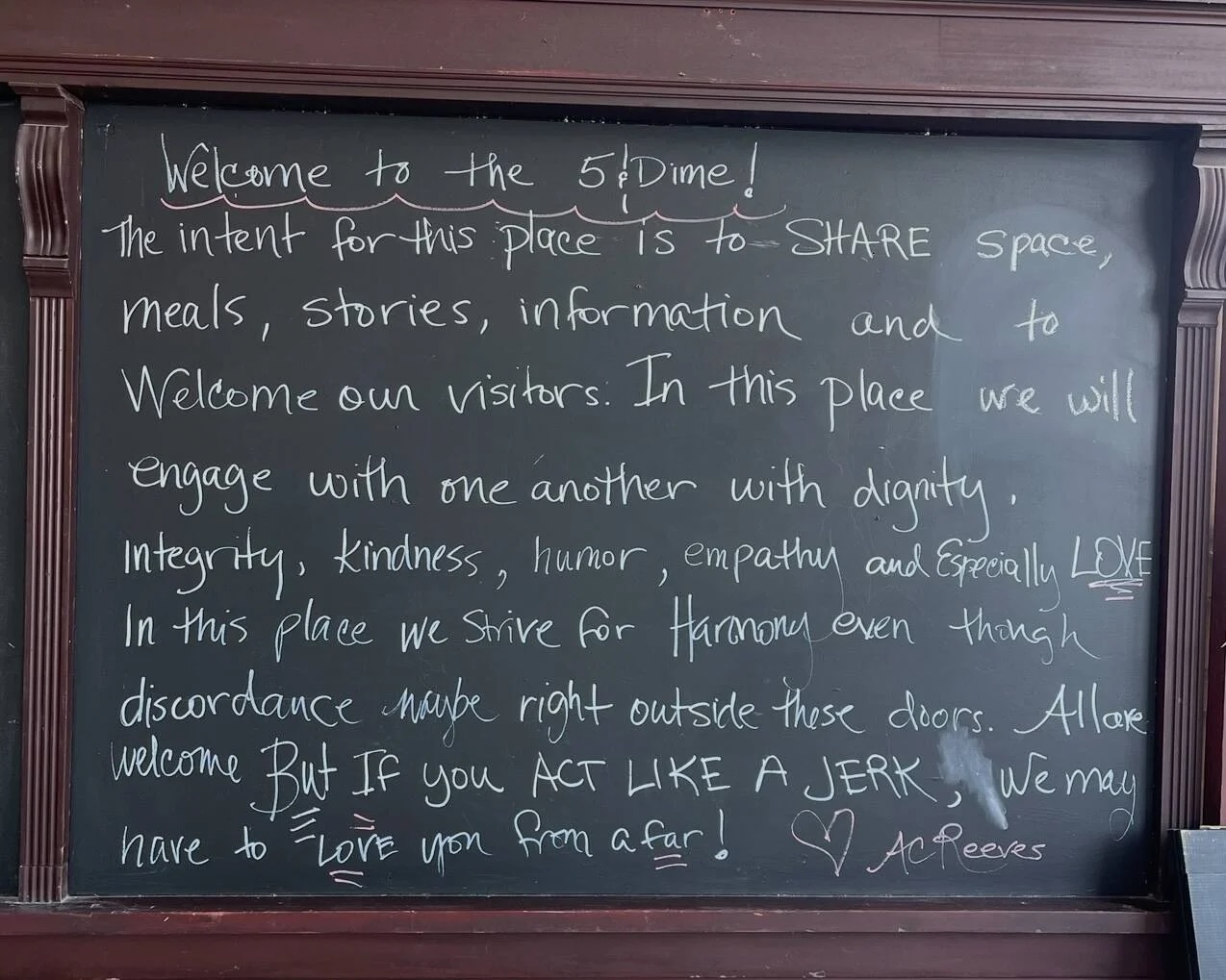 Blackboard reads "Welcome to the 5 & Dime! The intent for this place is to SHARE space, meals, stories, information and to welcome our visitors. In this place we will engage with one another with dignity, integrity, kindness, humor, empathy and especially LOVE. In this place we strive for harmony even though discordance maybe right outside these doors. All are welcome but if you act like a jerk, we may have to love you from afar! Love, AC Reeves