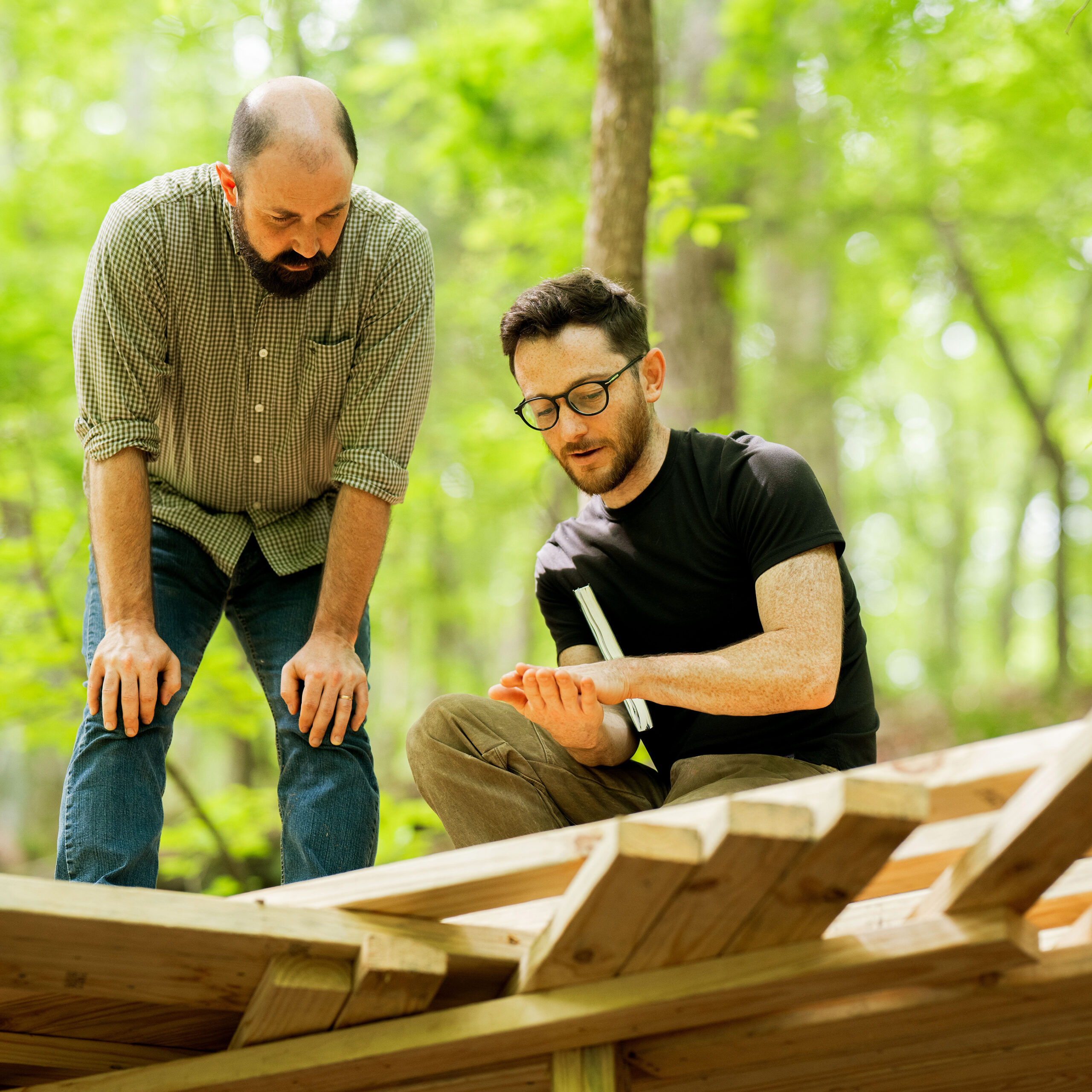 Stick Architecture@0.5x Charlie and Will in discussion while bending over a lumber project in the woods