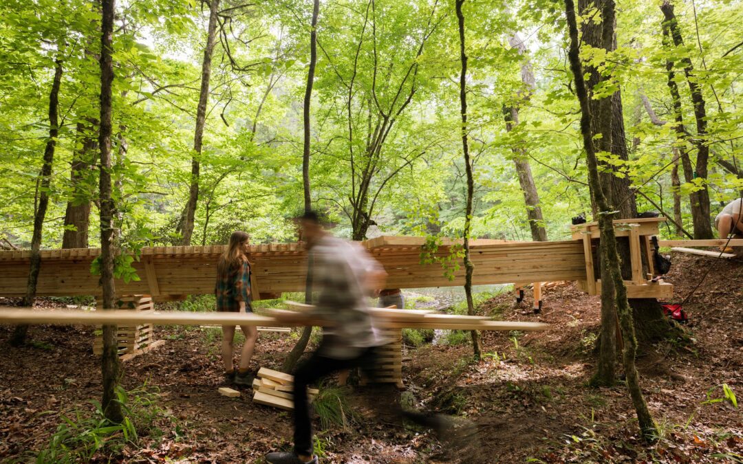 Bridge built from lumber in the woods as man carrying lumber runs past in a blur